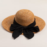 Tea colored colored straw hat with a thick black ribbon on a light beige background