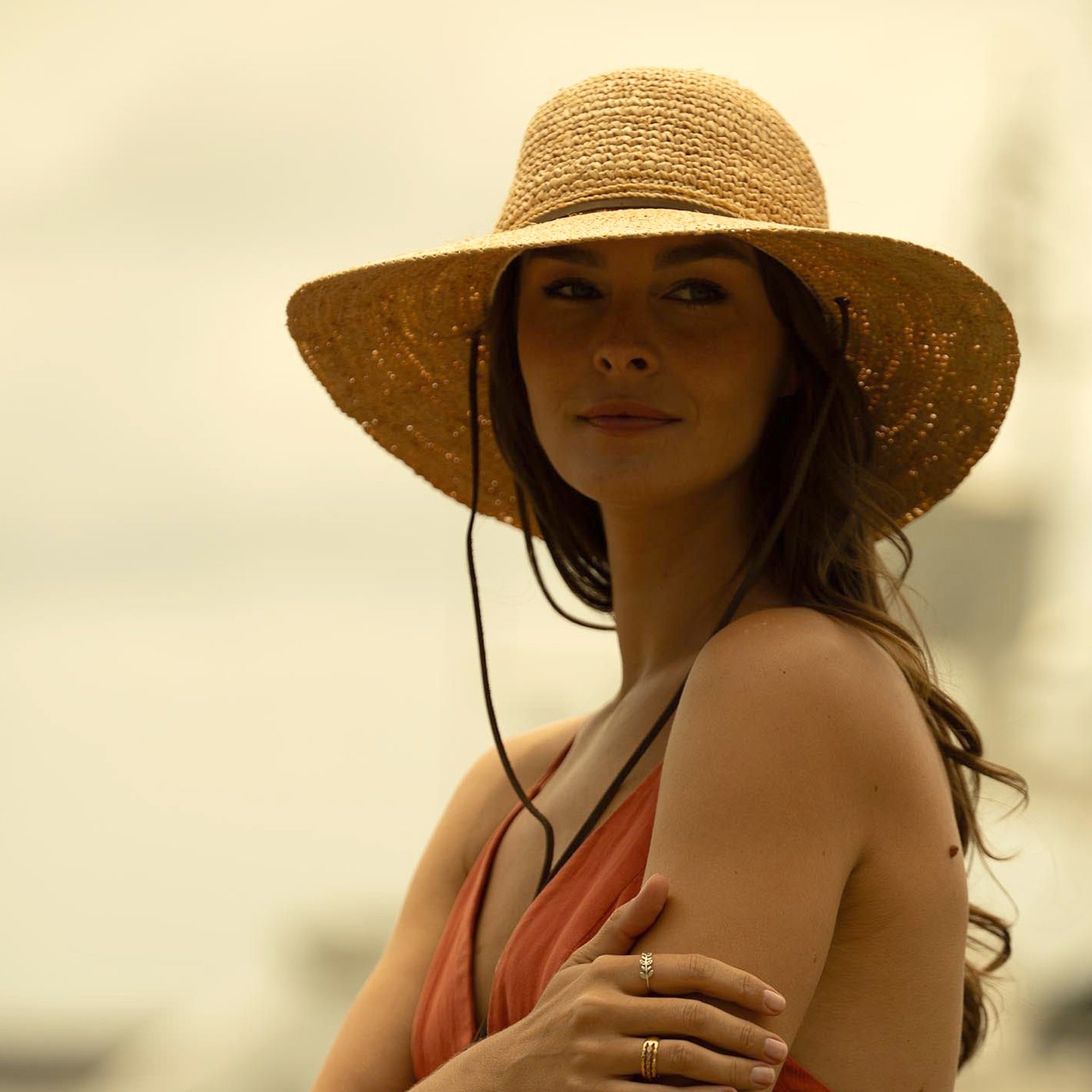 Woman wearing a natural colored straw hat and red top against a blurred natural background
