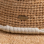 Close-up of a natural colored hat with a Scala logo pin and decorative rope-like band in dotted green, pink, gray, and white colors