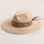 Natural colored straw hat with a brown band featuring white patterns on a light beige background