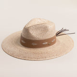 Natural colored straw hat with a brown band featuring white patterns on a light beige background
