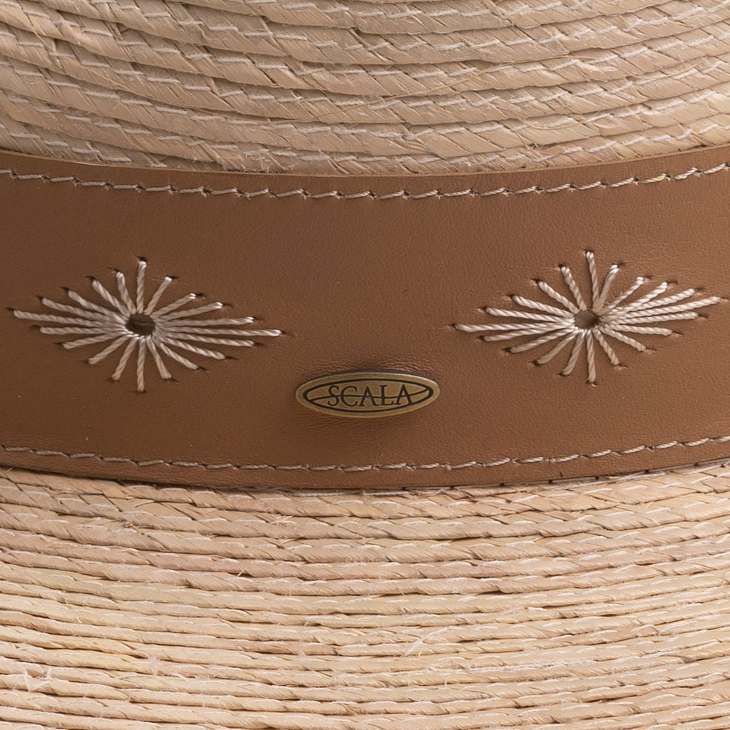 Close-up of a natural colored straw hat with decorative stitching and Scala logo pin on top of it