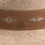 Close-up of a natural colored straw hat with decorative stitching and Scala logo pin on top of it