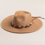 Toast colored straw hat with a decorative band on a light beige background