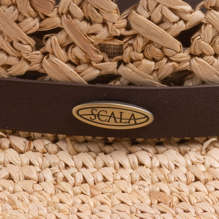 Close-up of a natural colored straw hat with a brown band and Scala logo pin on top of it