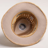 Underside of a natural colored straw hat with a golden colored sweatband on a light gray background