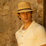 Man wearing a natural colored straw hat and light-colored shirt against a stone wall