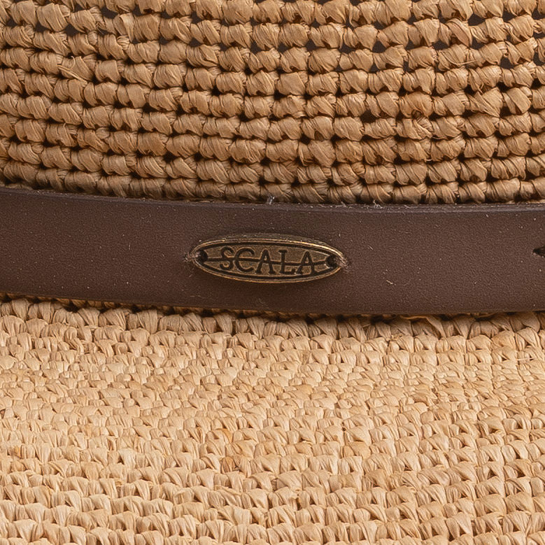 Close-up of a natural colored straw hat with a brown strap and Scala logo pin on top of it