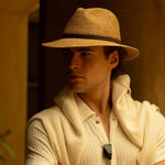 Man wearing a natural colored straw hat and light-colored outfit against a warm-toned background