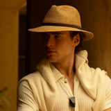 Man wearing a natural colored straw hat and light-colored outfit against a warm-toned background