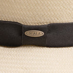 Close-up of a natural colored straw hat with a black band and Scala logo pin on top of it