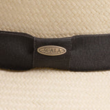 Close-up of a natural colored straw hat with a black band and Scala logo pin on top of it