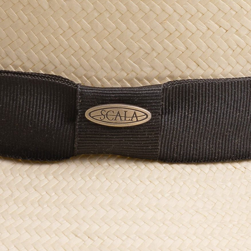 Close-up of a natural colored straw hat with a black band and Scala logo pin on top of it