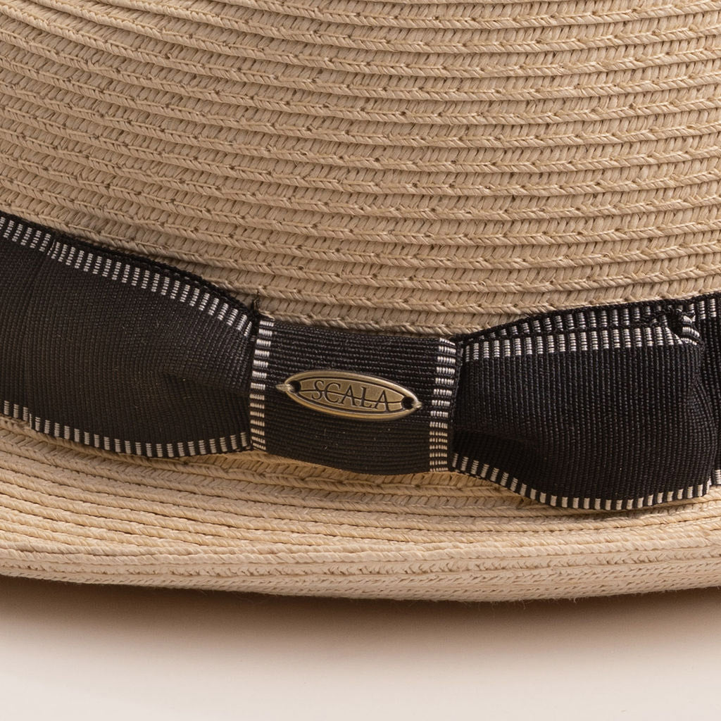 Close-up of a natural colored straw hat with a black ribbon and Scala logo pin on top of it