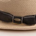 Close-up of a natural colored straw hat with a black ribbon and Scala logo pin on top of it
