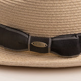 Close-up of a natural colored straw hat with a black ribbon and Scala logo pin on top of it