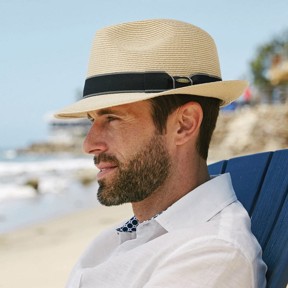 Man wearing a natural colored straw hat and white shirt sitting on a blue chair at the beach