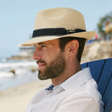 Man wearing a natural colored straw hat and white shirt sitting on a blue chair at the beach