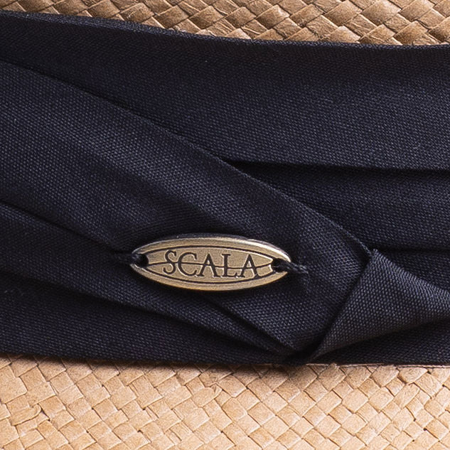 Close-up of a putty colored straw hat with a black band featuring the Scala logo pin on top of it