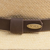 Close-up of a natural colored Panama hat with a brown band featuring the Scala logo pin on top of it