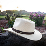 Natural colored Panama hat with a brown band on a stone surface with a garden background