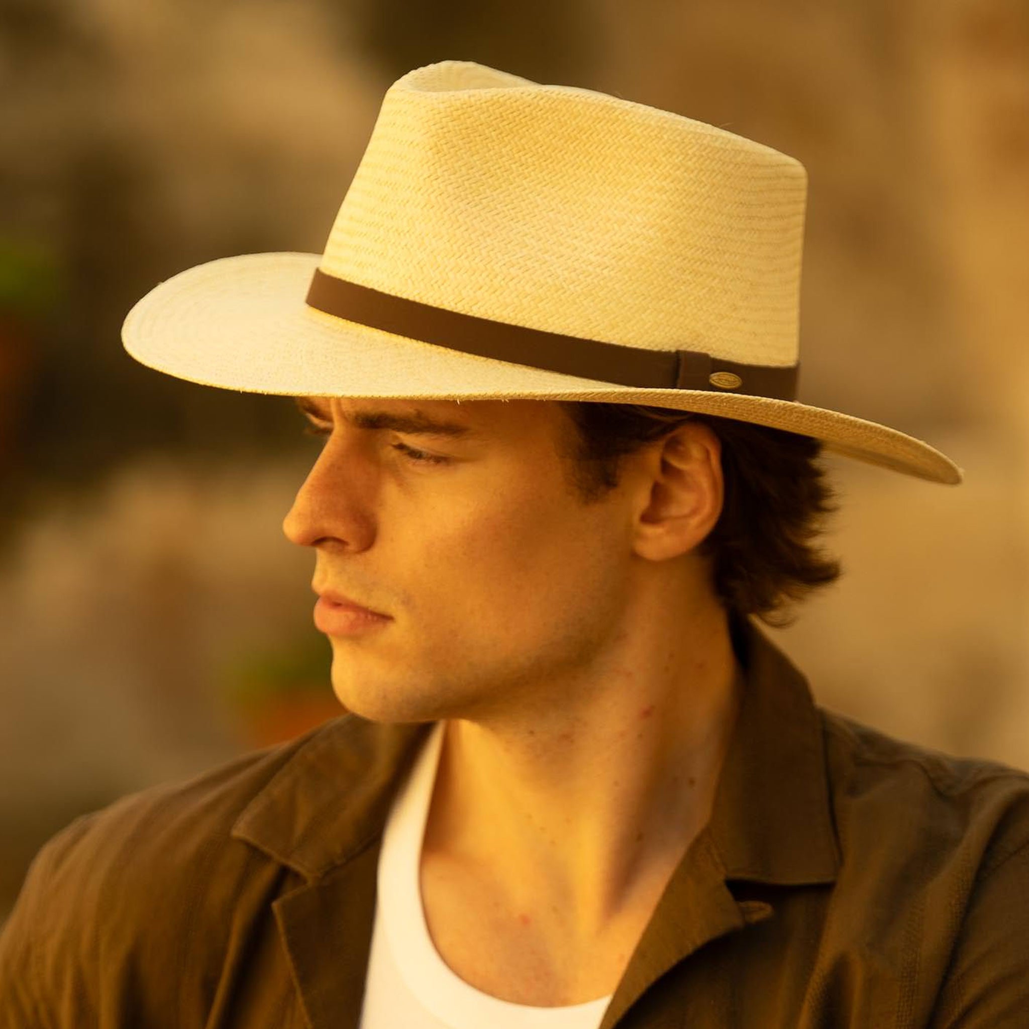 Man wearing a natural colored Panama hat with a brown band against a blurred natural background