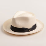 Bleach colored Panama hat with a thick black band on a light beige background