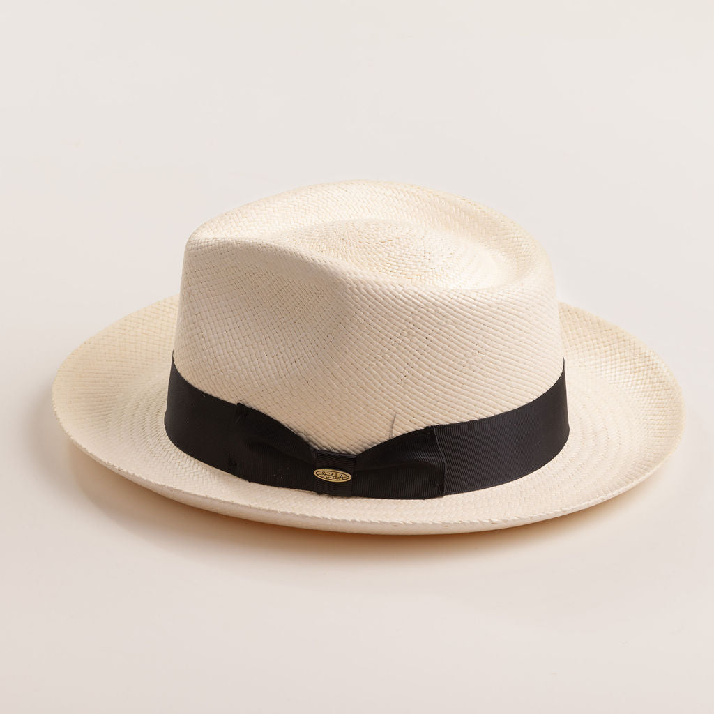 Bleach colored Panama hat with a thick black band on a light beige background