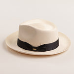 Bleach colored Panama hat with a thick black band on a light beige background