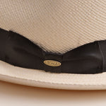 Close-up of a bleach colored Panama hat with a thick black band and Scala logo pin on top of it