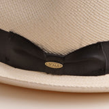 Close-up of a bleach colored Panama hat with a thick black band and Scala logo pin on top of it