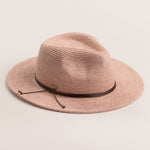 Blush colored straw hat with a brown band on a light beige background