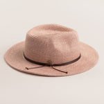 Blush colored straw hat with a brown band on a light beige background