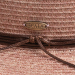 Close-up of a blush colored straw hat with a knotted string and Scala logo pin
