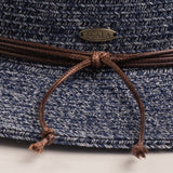 Close-up of a denim colored straw hat with a knotted string and Scala logo pin