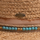 Close-up of a natural colored straw hat with a decorative band featuring turquoise beads and gold accents, with a Scala logo pin