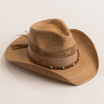 Tea colored straw-shaped cowboy hat with decorative band with turquoise beads on a light beige background
