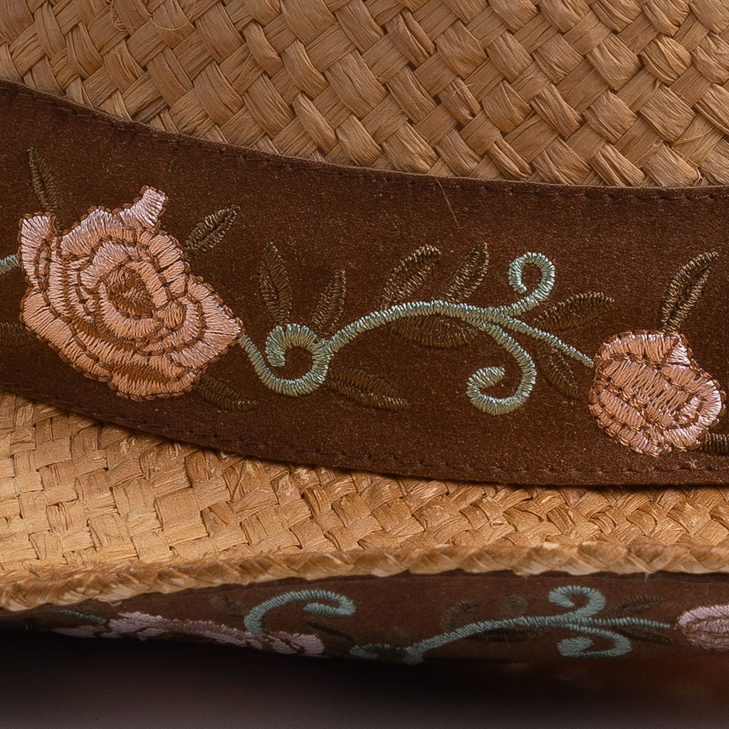 Close-up of a tea colored straw hat with embroidered floral band and underbrim
