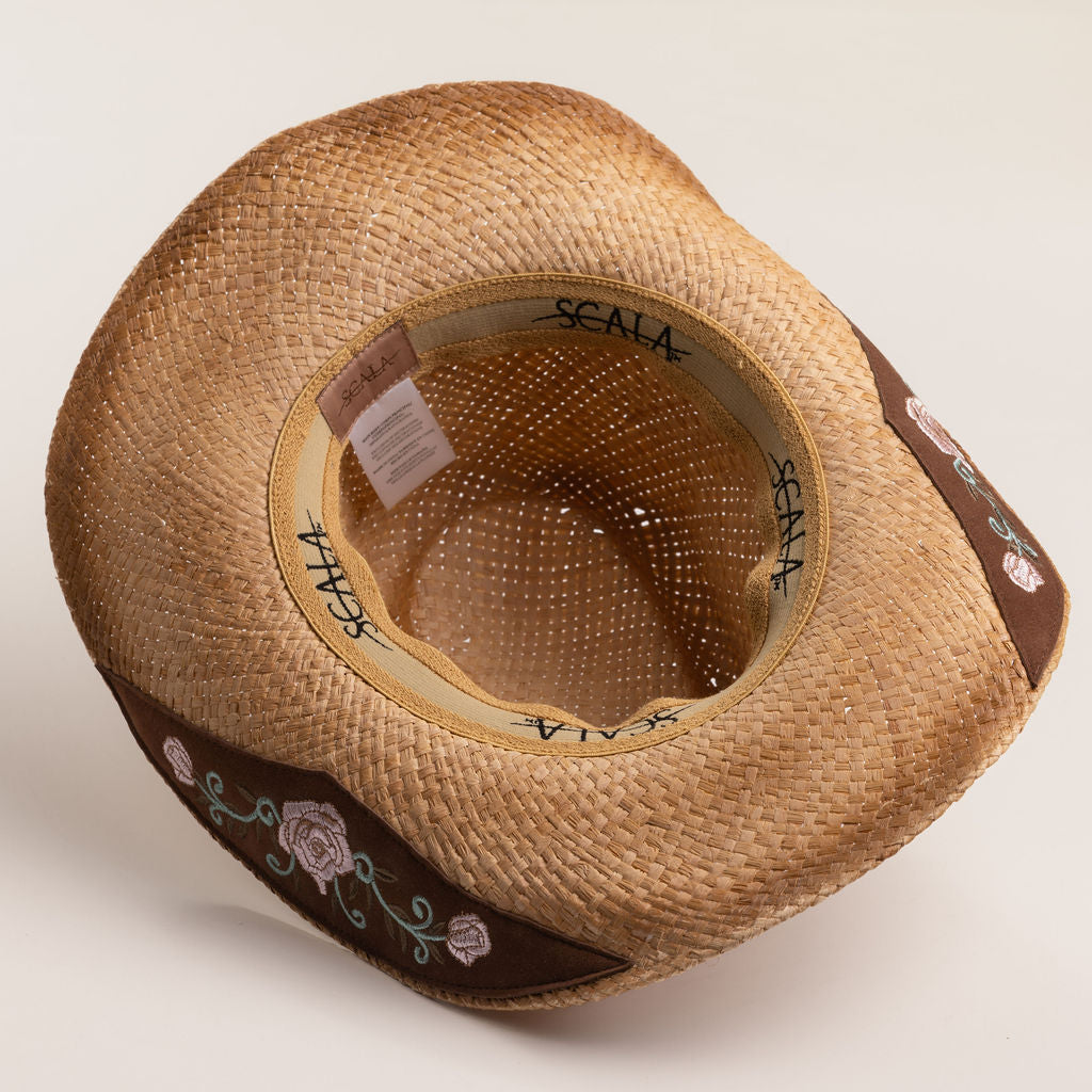 Underside of a tea colored straw cowboy-shaped hat with decorative floral pattern underbrim on a light beige background