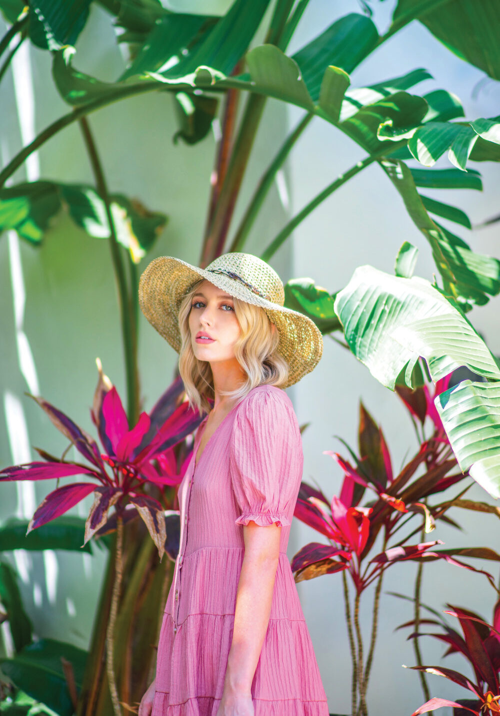 Woman in a pink dress and straw hat standing among tropical plants