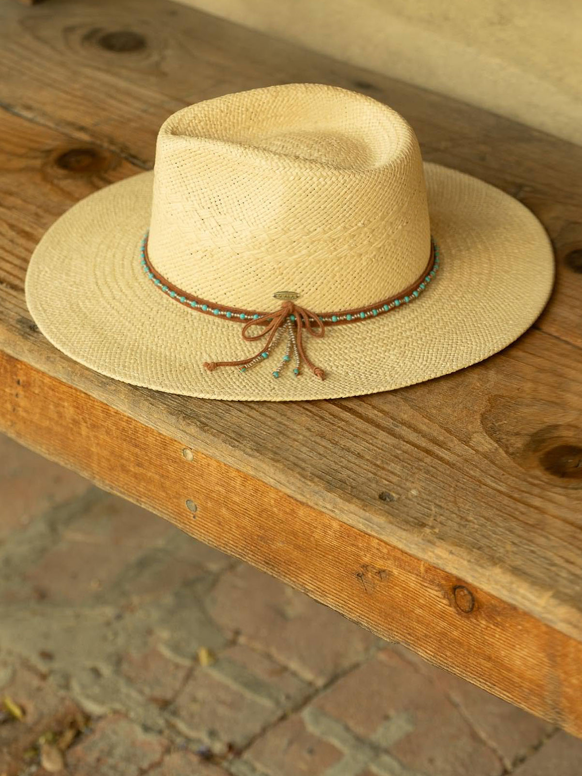 Beige straw hat with a decorative turquoise and brown band resting on a flat wooden surface