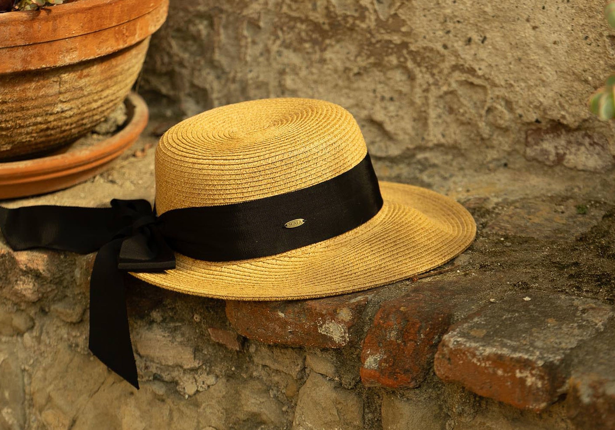 Natural colored straw hat with a thick black ribbon on a stone surface