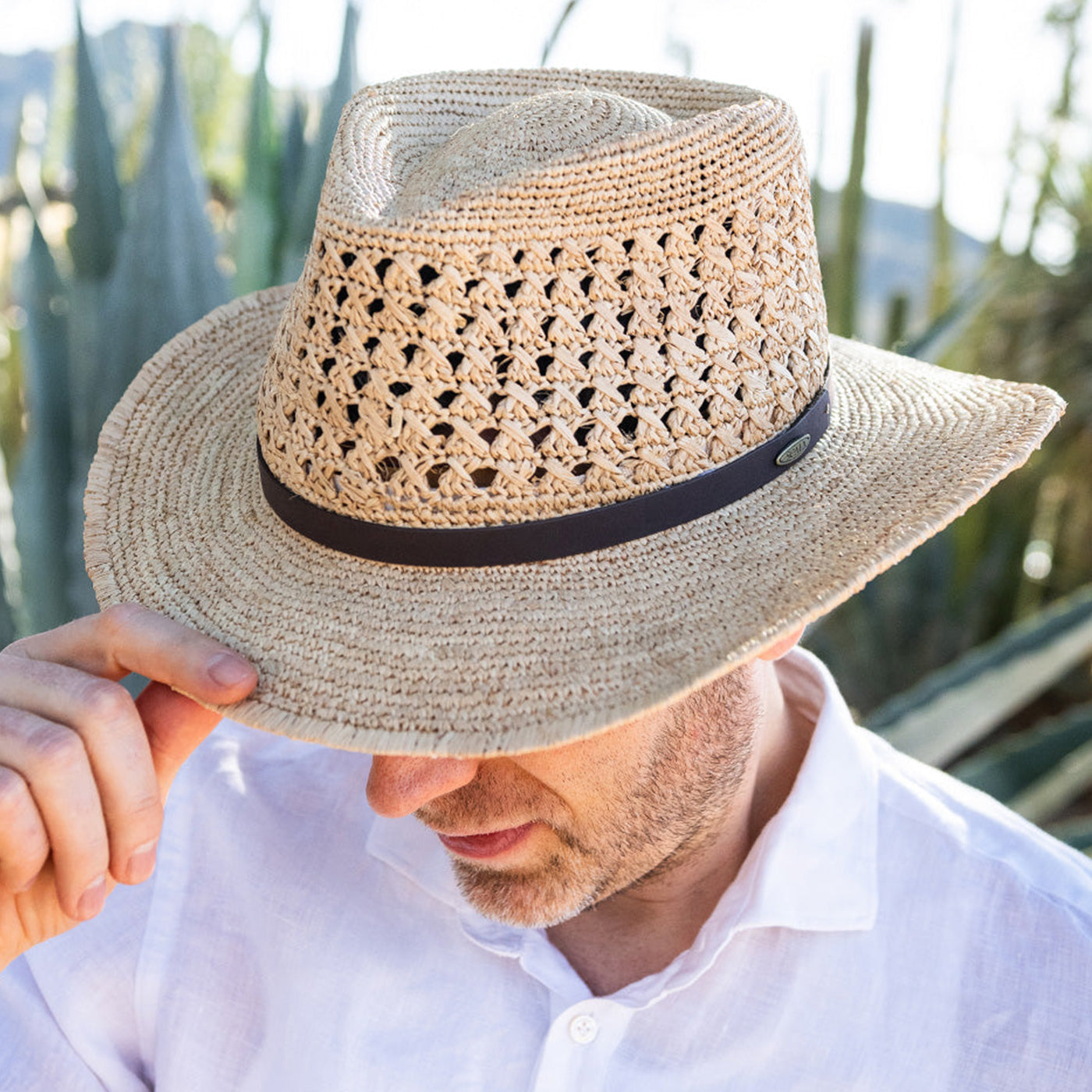 Man wearing a bright golden colored hat, striped shirt, and white undershirt sitting on steps with his left arm pointing upwards while resting on his thigh
